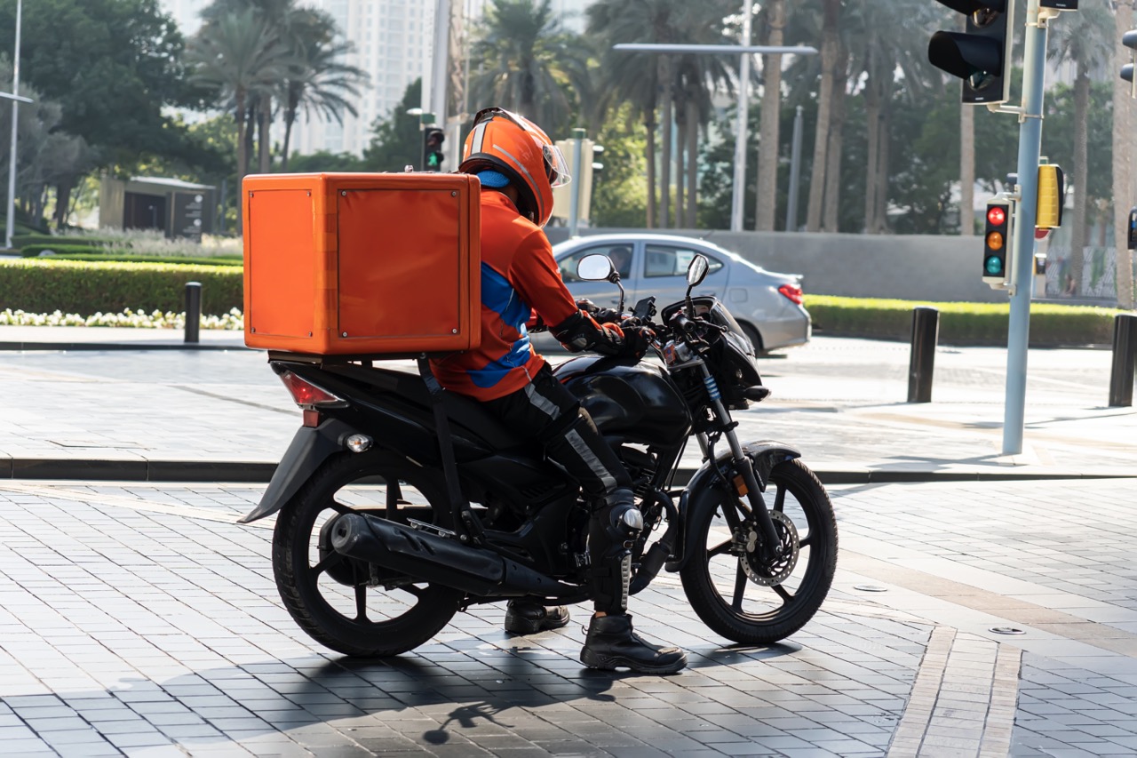motorbike delivery man wearing orange uniform ready to send food. delivering food. delivery man of take away with isothermal food pink case box driving find home. express food delivery service.